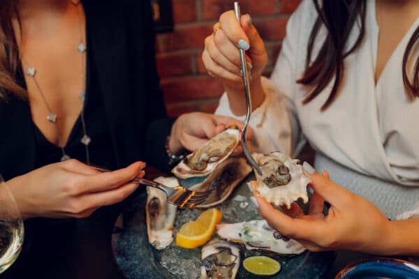 hands holding oysters with other seafood dishes on a dark table